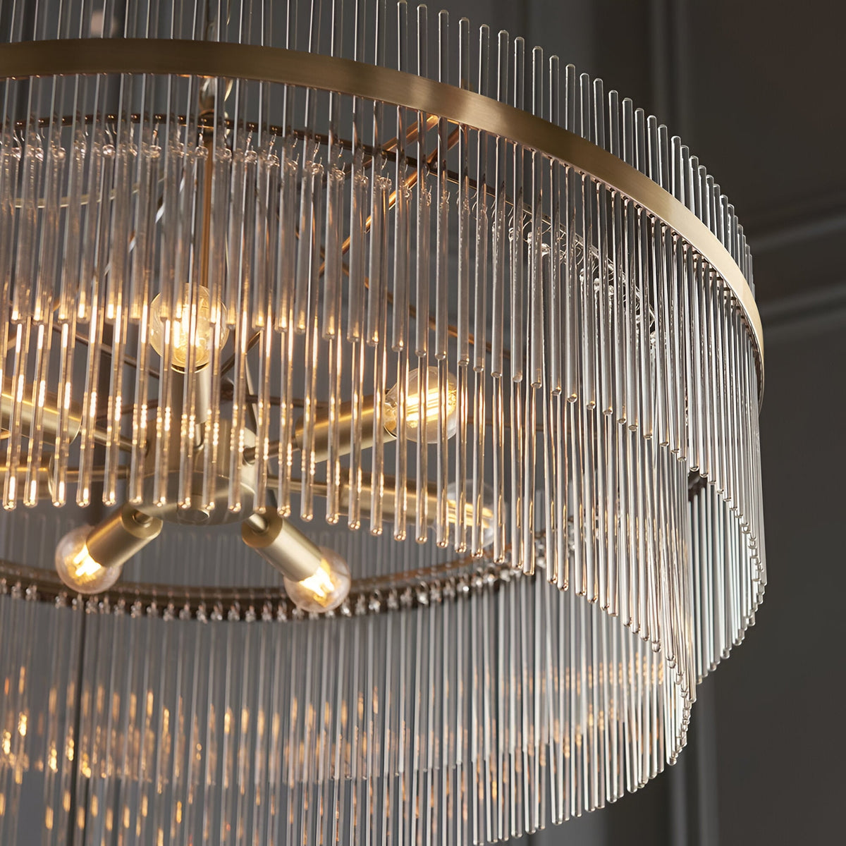 Close-up of Endon Beaumont 7 Light Pendant in antique brass, showing lit E14 lamps, tiered rings and clear glass rod fringing.