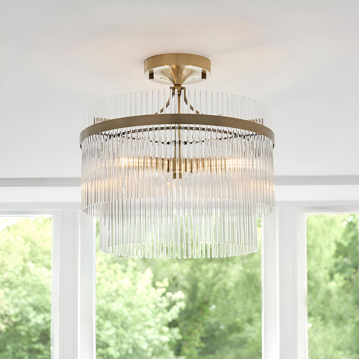 Endon Beaumont 3 light semi-flush ceiling light in brass with two tiered rows of clear glass rods, mounted to a white ceiling between bright windows.