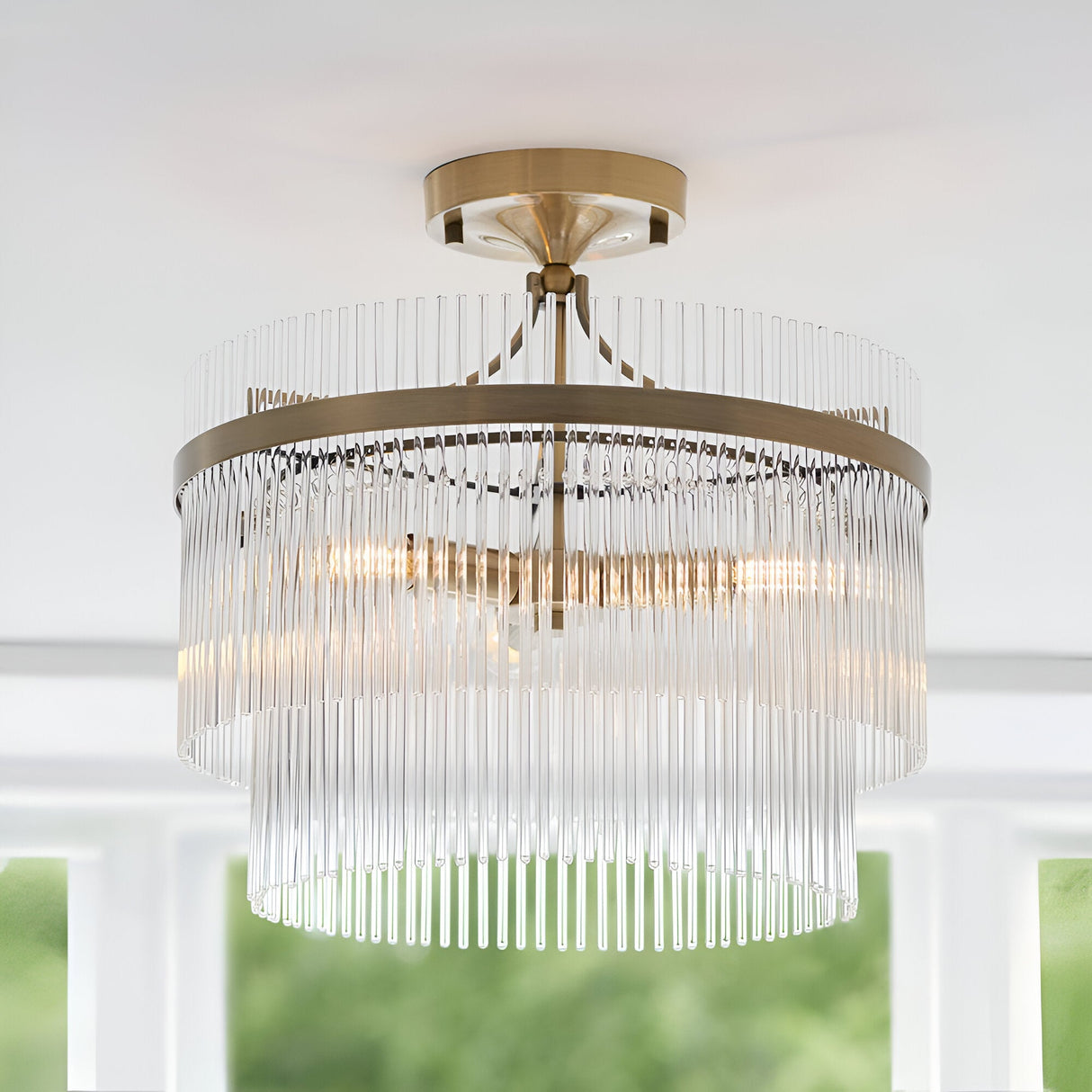 Endon Beaumont 3 light semi-flush ceiling light in brass with tiered clear glass rod fringes, mounted to a white ceiling near a bright window.