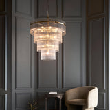 Beaumont 16 Light Chandelier in antique brass with tiered clear glass rods, hung above a table and armchair in a dark panelled room.