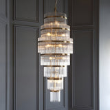 Endon Beaumont 21 light chandelier in antique brass with multi-tiered clear glass rods, hung from a chain against a grey panelled wall.