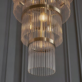 Close-up of Endon Beaumont 21 Light Chandelier in antique brass with tiered clear glass rods and lit E14 bulbs against a grey panelled wall.
