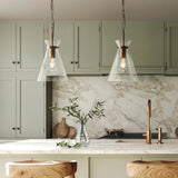 Endon Brenbury pendant lights in brushed brass with clear glass conical shades and exposed bulbs, hung as a pair above a marble kitchen island.