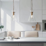 Two Endon Brenbury pendant lights in brushed brass with clear tapered glass shades, suspended by chains above a white kitchen island with boucle stools.
