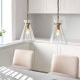 Endon Brenbury pendant lights in brushed brass with clear tapered glass shades and exposed E27 bulbs, hung on chains above a kitchen dining area.