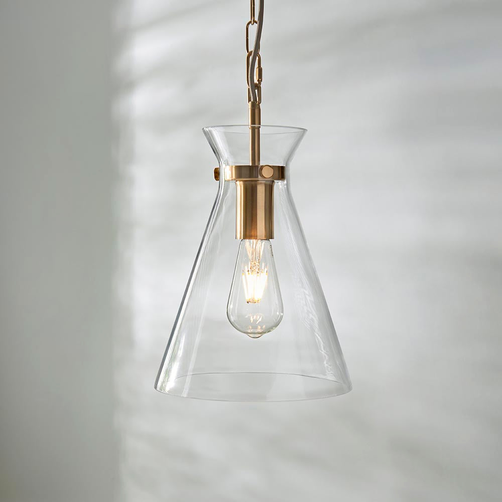 Endon Brenbury pendant light with a clear tapered glass shade, brushed brass fitting and exposed E27 filament bulb, hung against a soft neutral wall.