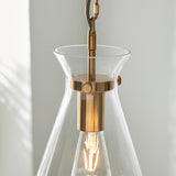 Close-up of the Endon Brenbury pendant showing its brushed brass fitting, clear tapered glass shade, exposed E27 filament bulb and grey fabric cable.