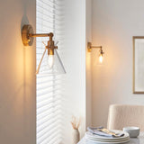 Endon Brenbury antique brass wall light with clear glass shade and exposed bulb, shown beside a window with a second matching sconce on the wall opposite.