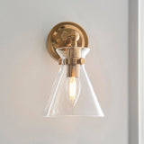 Endon Brenbury wall light with brushed antique brass fitting, adjustable knuckle and clear glass cone shade around an exposed E14 bulb, on a pale wall.