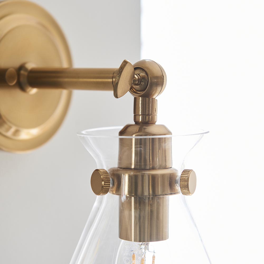 Close-up of the Endon Brenbury wall light in antique brushed brass, showing the adjustable knuckle, thumbscrews and clear glass shade with exposed bulb.