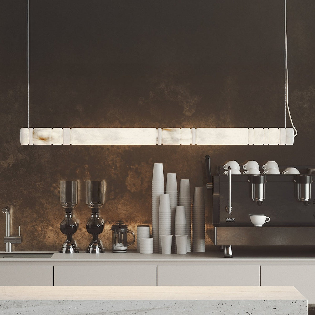 Bowie LED Alabaster Linear Pendant Light, a slim sectioned alabaster bar suspended above a dark café counter with cups and an espresso machine.