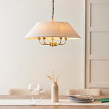 Caldmere 5-Light Pendant in brass and natural linen with a wide tapered shade, hung above a dining table with chairs, vase, and glassware.
