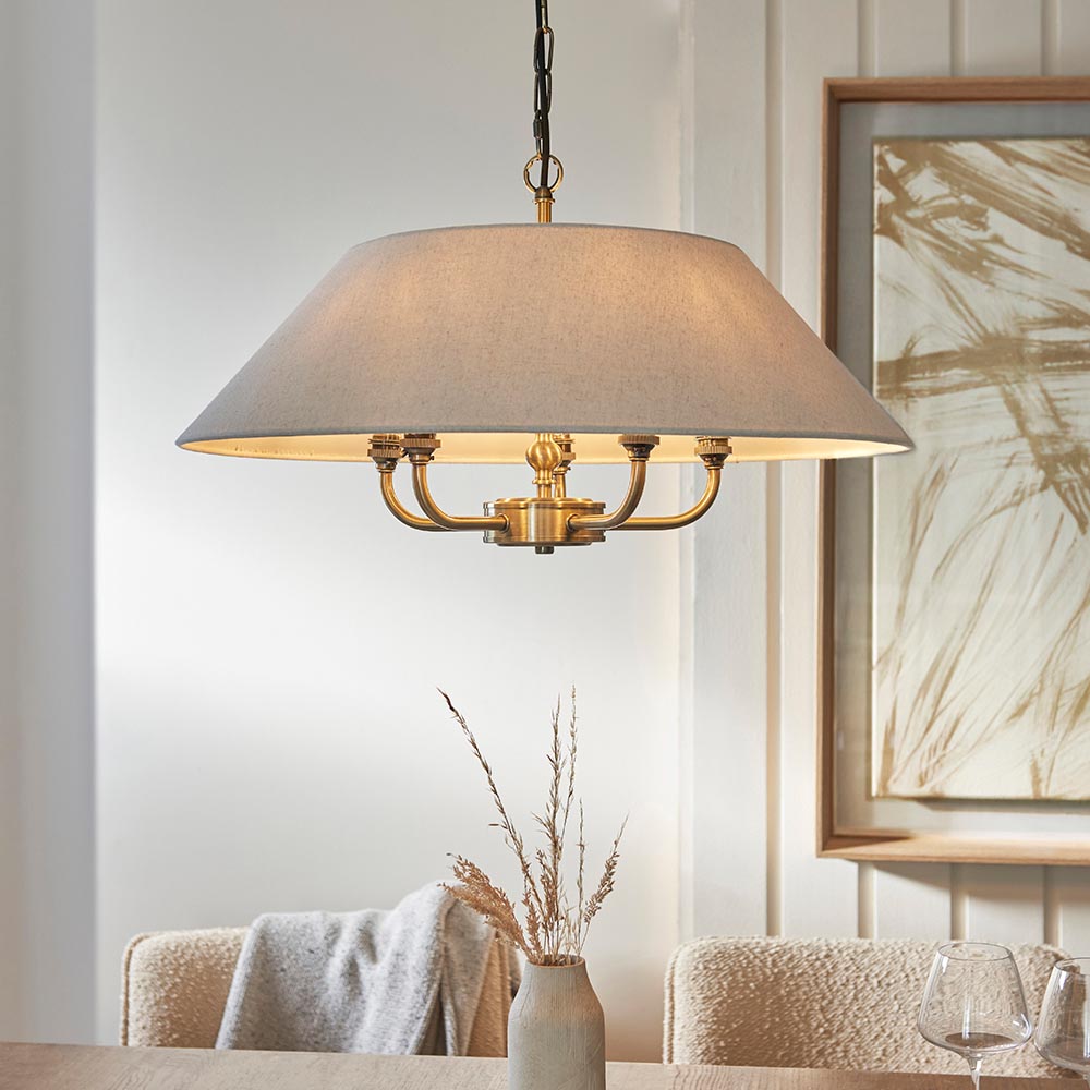 Caldmere 5 Light Pendant with brass frame and natural fabric drum shade, hung by black chain above a dining table.
