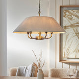 Caldmere 5 Light Pendant with brass frame and natural fabric drum shade, hung by black chain above a dining table.