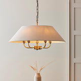 Caldmere 5 Light Pendant in brass with a wide natural fabric drum shade, suspended from a chain, shown in a room setting with a vase nearby.