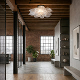 Modern industrial loft with exposed brick walls, grid windows, wood ceiling beams, concrete floor, minimalist furniture, plants, abstract art, and a striking sculptural fixture featuring the Violla LED Flush Ceiling Light - White.