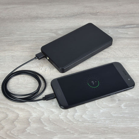 AVSL AV:Link USB3.0 Type-A to Type-C 1.5m cable charging a black smartphone displaying 57% from a black power bank on a light wood surface.