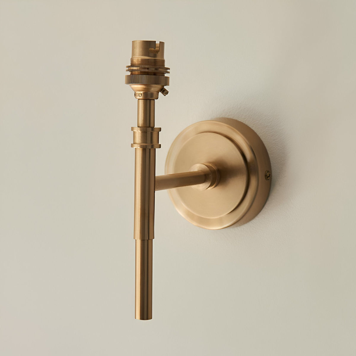 Endon Bevford wall light in aged brass, compact fitting with a slim stem, B22 lampholder and round wall plate, shown against a pale background.