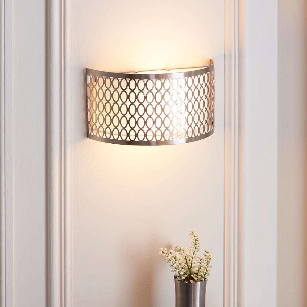 Endon Rosaline 2 light wall light in satin nickel with geometric fretwork and white inner shade, illuminated on a panelled wall above a small floral vase.