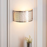 Endon Rosaline 2 light wall light in satin nickel with geometric fretwork and white inner shade, illuminated on a panelled wall above a small floral vase.