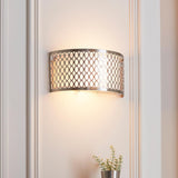 Endon Rosaline 2 light wall light in satin nickel with geometric fretwork, white fabric inner shade and frosted glass diffusers, lit on a panelled wall.