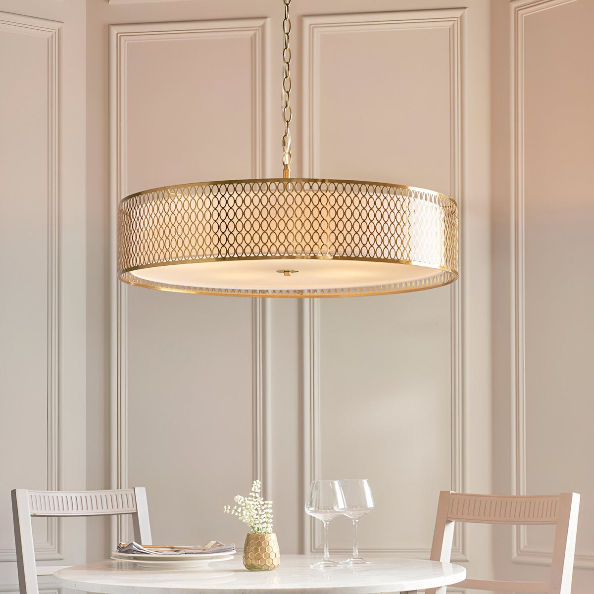 Rosaline 5-Light Pendant in gold and white, a large drum fixture with geometric fretwork shade and frosted glass diffuser, hung above a dining table.