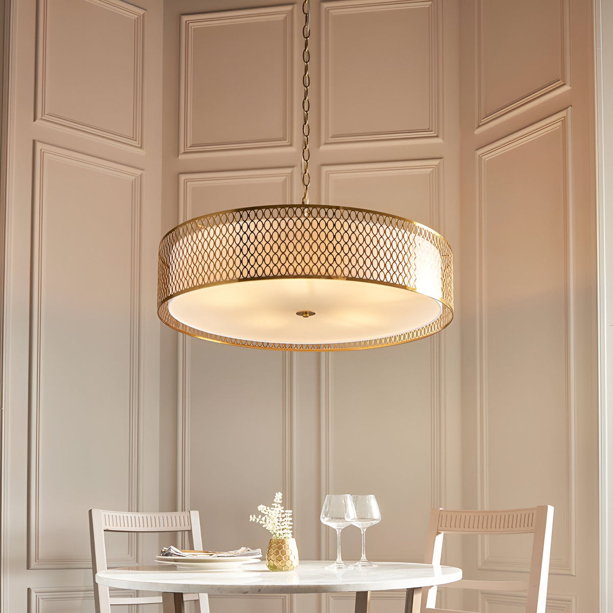 Rosaline 5-Light Pendant in gold and white, a drum-shaped fixture with geometric metal fretwork and a frosted glass diffuser, hung above a dining table.