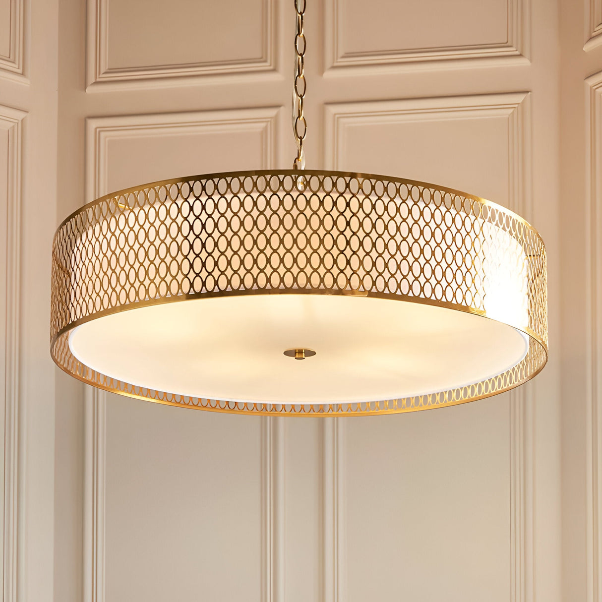 Rosaline 5 Light Pendant in gold and white, large drum shade with geometric fretwork exterior and frosted glass diffuser, hung from a chain in a panelled room.