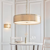 Rosaline 5-Light Pendant in gold and white with a large drum shade, geometric fretwork, white fabric inner, and frosted glass diffuser, above a dining table.