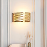 Rosaline 2-light wall light in gold with curved geometric fretwork, illuminated on a wall between panelled mouldings above a vase of dried grasses.