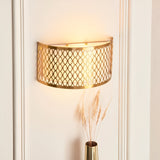 Rosaline 2 Light Wall Light in gold with geometric fretwork outer and white fabric inner shade, mounted on a wall beside a vase with dried grasses.