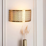 Rosaline 2 Light Wall Light in gold with geometric metal fretwork and white fabric inner shade, mounted on a wall above a vase in a hallway setting.