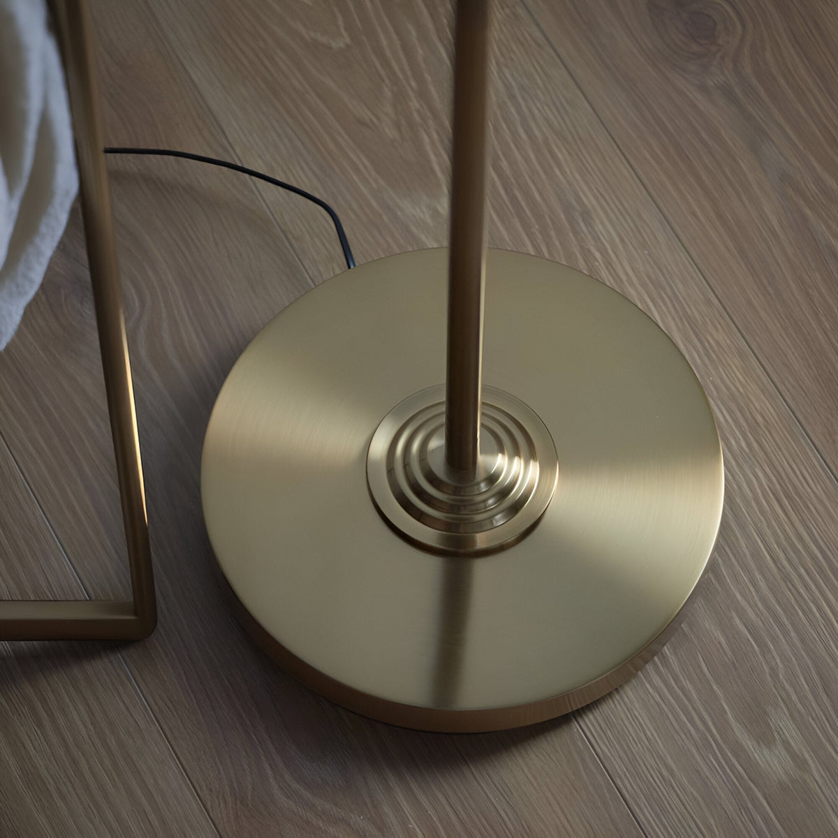 Close-up of the Brenley Floor Lamp's round brass base with concentric ring detailing and central rod, on a wooden floor.