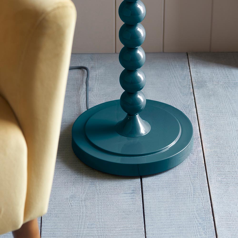 Endon Brenleigh floor lamp base in glossy marlin blue, with stacked metal spheres on a round disc base, shown beside a yellow armchair on grey plank flooring.