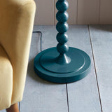 Endon Brenleigh floor lamp base in glossy marlin blue, with stacked metal spheres on a round disc base, shown beside a yellow armchair on grey plank flooring.