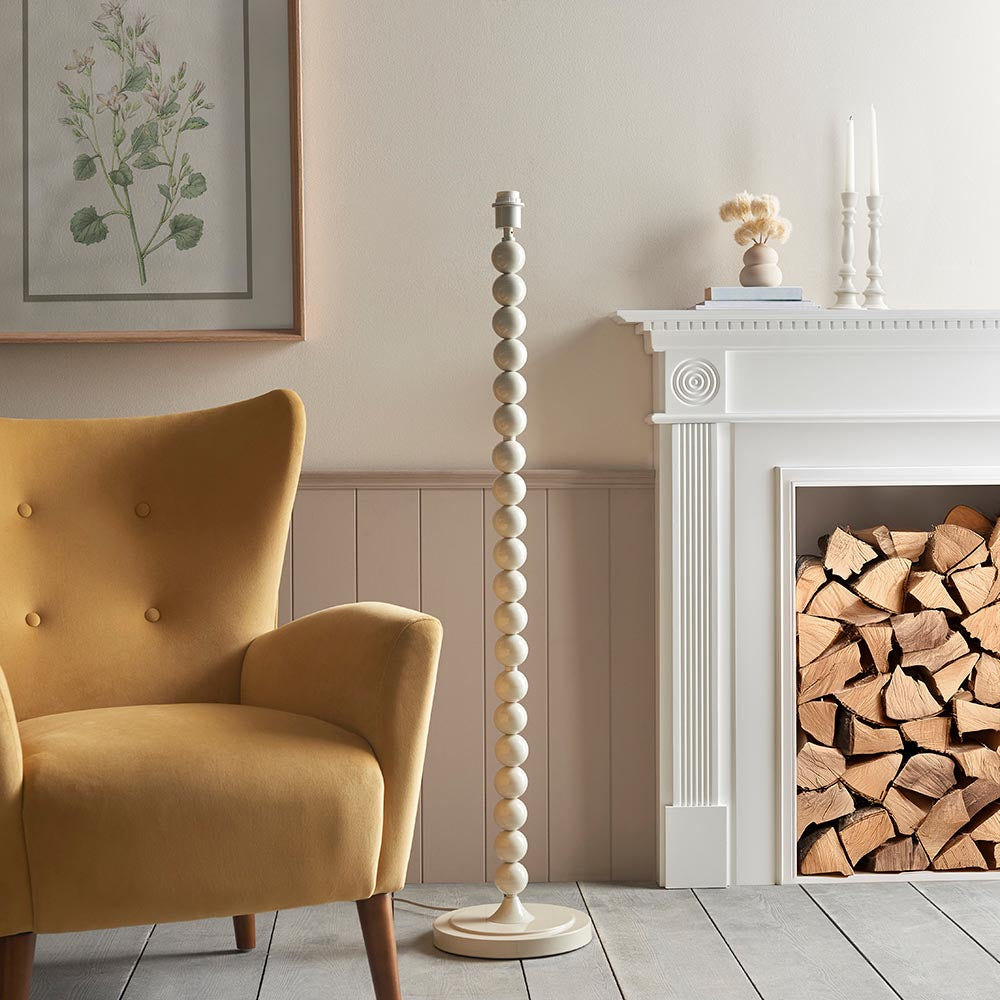 Endon Brenleigh floor lamp base in white with stacked glossy metal spheres, shown beside a mustard armchair and white fireplace in a living room.