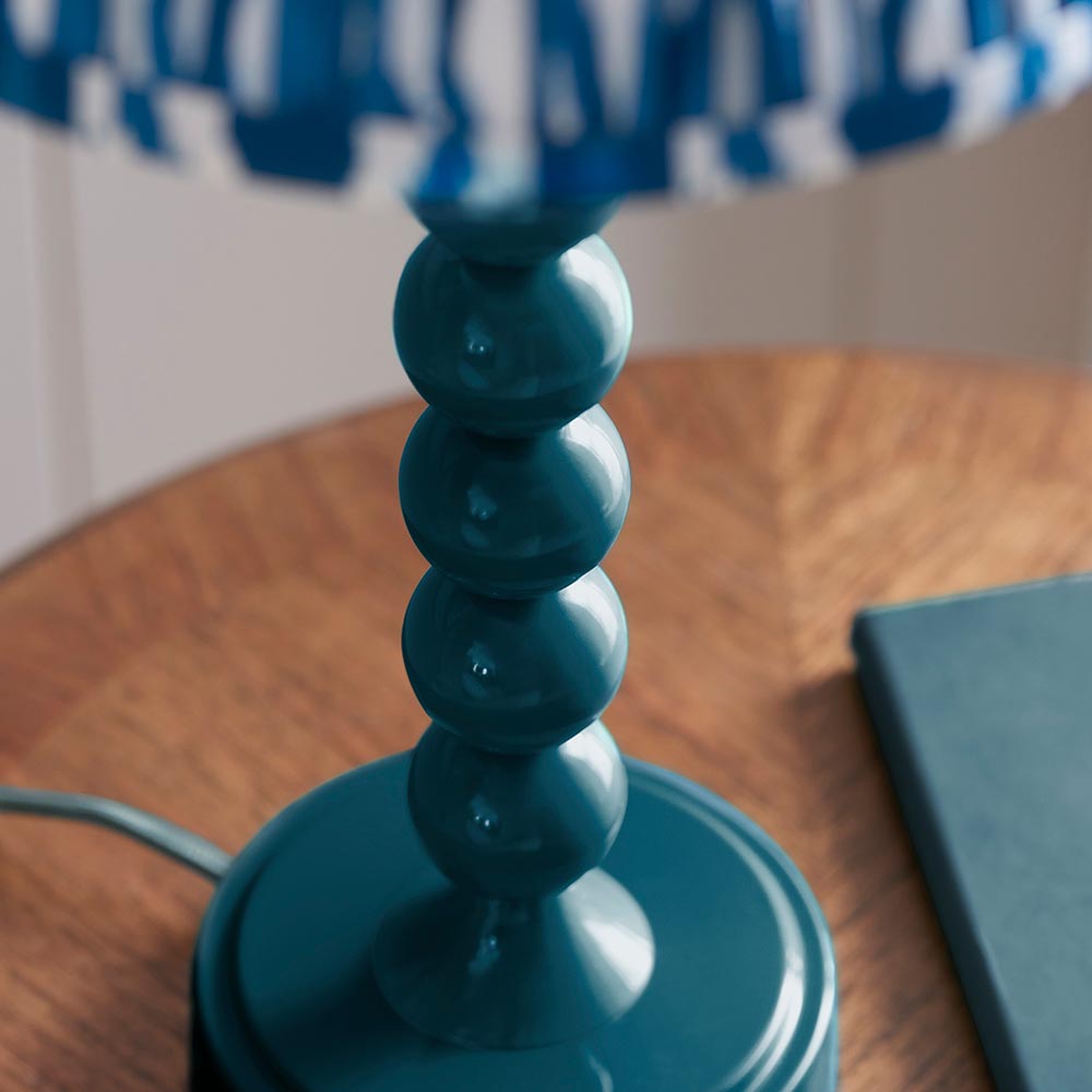 Brenleigh Table Lamp in blue, close-up of the stacked glossy metal sphere base with patterned fabric shade, set on a wooden table.