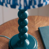 Brenleigh Table Lamp in blue, close-up of the stacked glossy metal sphere base with patterned fabric shade, set on a wooden table.