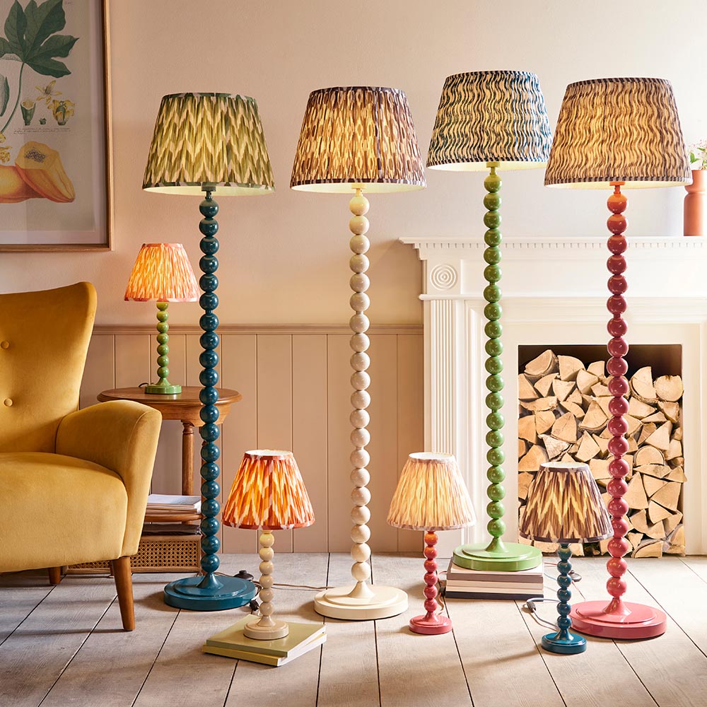 Endon Brenleigh table lamps with stacked sphere bases in blue, cream, green and pink, with patterned fabric shades, styled by a fireplace and armchair.