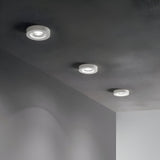 A ceiling showcasing three Eden Round Recessed Downlights - White, evenly spaced in a linear arrangement, brightening a minimalist room with light gray walls and a subtly textured ceiling. These lights each include dimmable GU10 bulbs, providing adaptable lighting to suit any occasion.