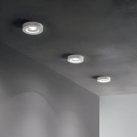 A ceiling showcasing three Eden Round Recessed Downlights - White, evenly spaced in a linear arrangement, brightening a minimalist room with light gray walls and a subtly textured ceiling. These lights each include dimmable GU10 bulbs, providing adaptable lighting to suit any occasion.