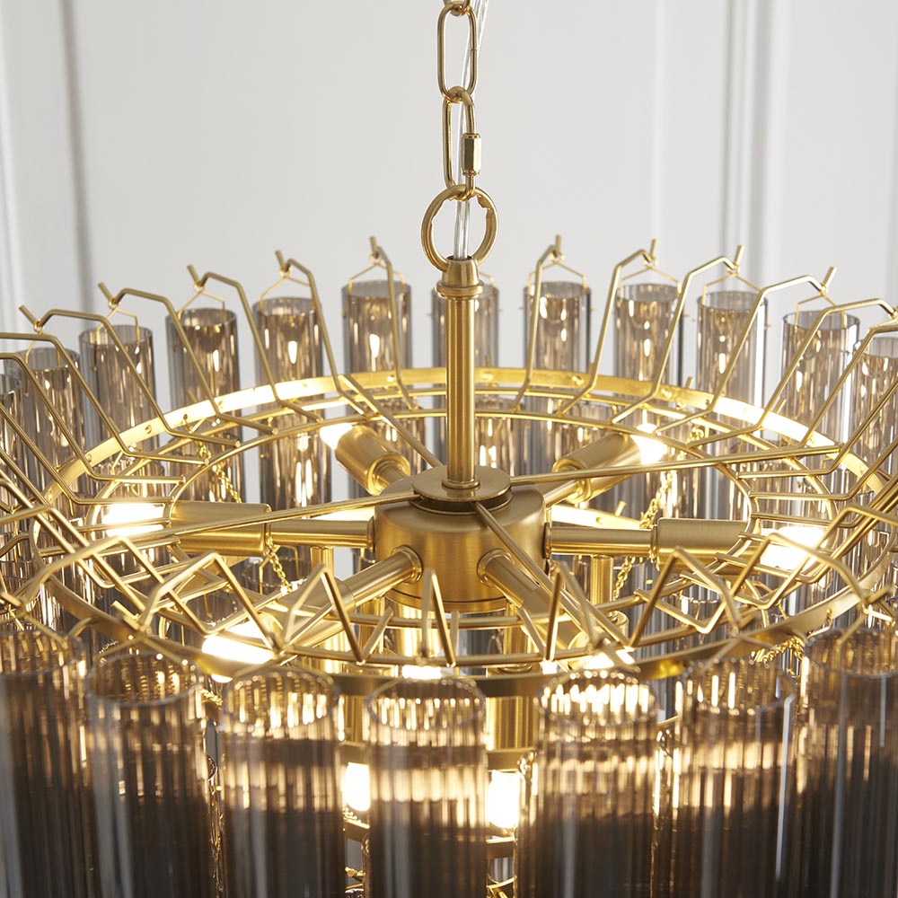 Close-up of Endon Cranshaw 12 Light Tiered Pendant in satin brass with smokey grey glass tubes, showing the frame, chain suspension and illuminated G9 lamps.