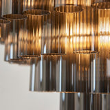 Close-up of Endon Cranshaw 12 Light Tiered Pendant showing smokey grey ribbed glass cylinders suspended from a satin brass frame.