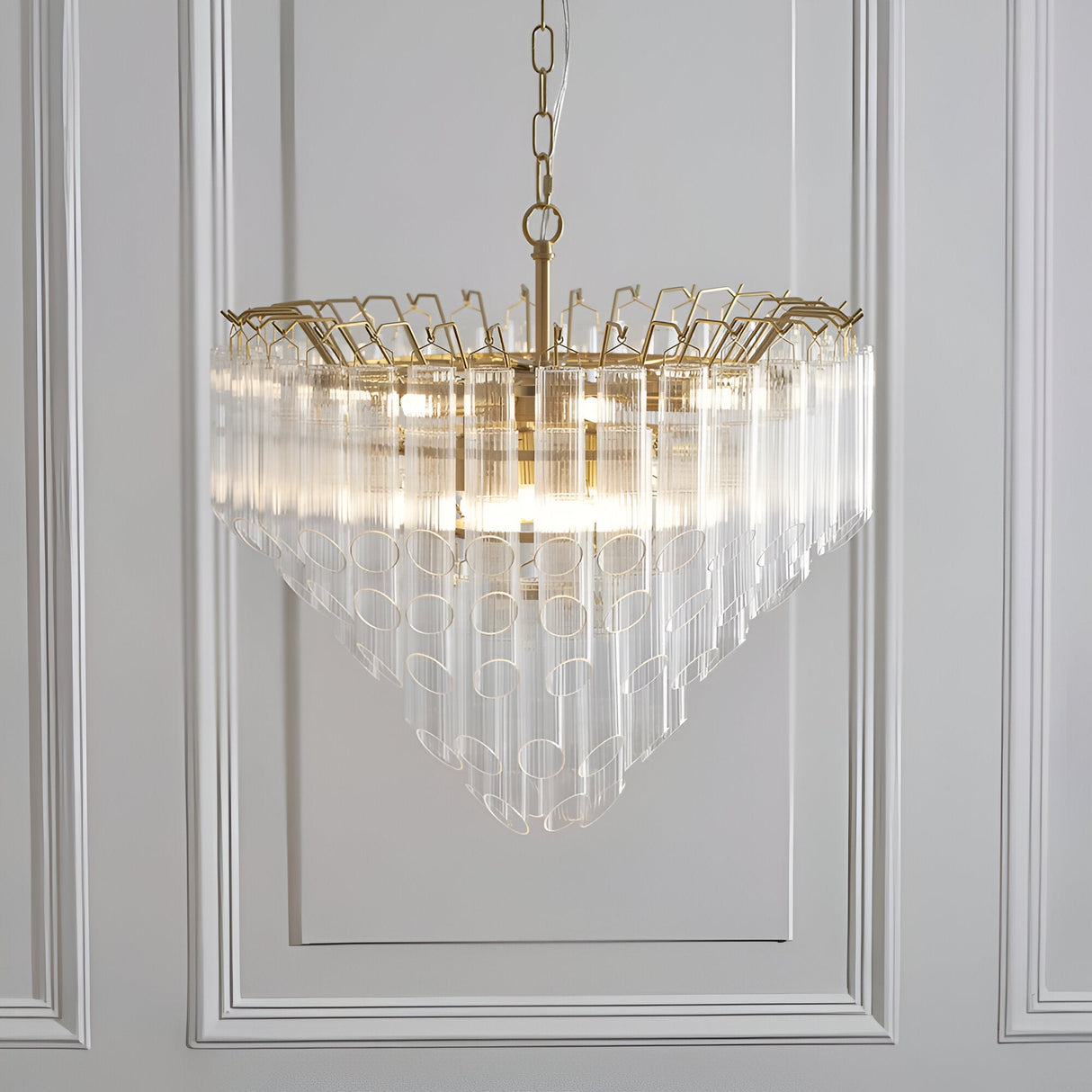 Cranshaw 12 Light Tiered Pendant in satin brass with clear ribbed glass rods, hung from a chain against a panelled white wall.