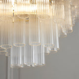 Close-up of the Endon Cranshaw 12 light tiered pendant showing ribbed clear glass cylinders layered on satin brass metalwork with warm glowing lamps above.