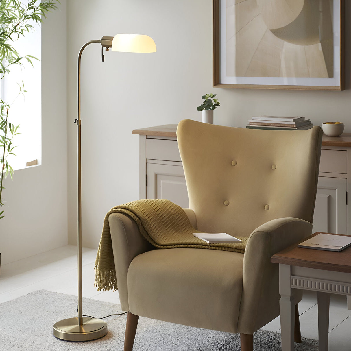 Endon Chartbourne floor lamp with antique brass stem and gloss opal glass shade, beside a mustard velvet wingback armchair in a neutral living room.
