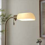 Endon Chartbourne floor lamp close-up showing the antique brass tilting head with gloss opal glass shade illuminated beside a framed print.
