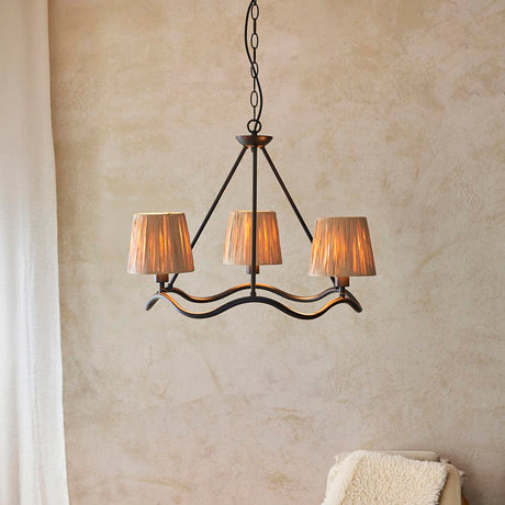 Endon Danemont 3 Light Pendant in black with a wave-shaped hoop and three hand-wrapped raffia tapered shades, hung from a chain against a plaster wall.
