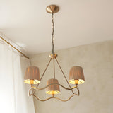 Danemont 3 Light Pendant in brass with a wave-shaped hoop and hand-wrapped raffia shades, hanging from a chain in a softly lit room.