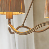 Close-up of the Danemont 3 Light Pendant in brass, showing the wave-shaped metal hoop and a hand-wrapped raffia shade against a soft neutral background.